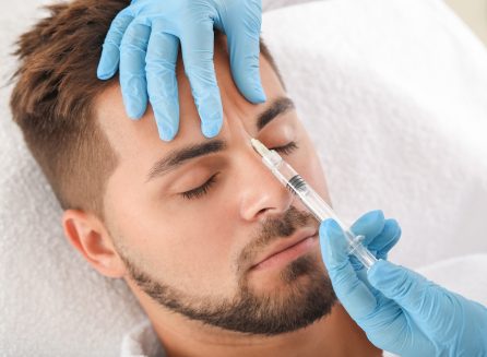 Handsome man receiving filler injection in beauty salon