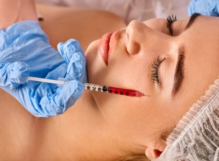 Close-up of a patient receiving an aesthetic under-eye treatment with a precision syringe. A professional wearing blue gloves performs the procedure for facial rejuvenation and dark circle correction.